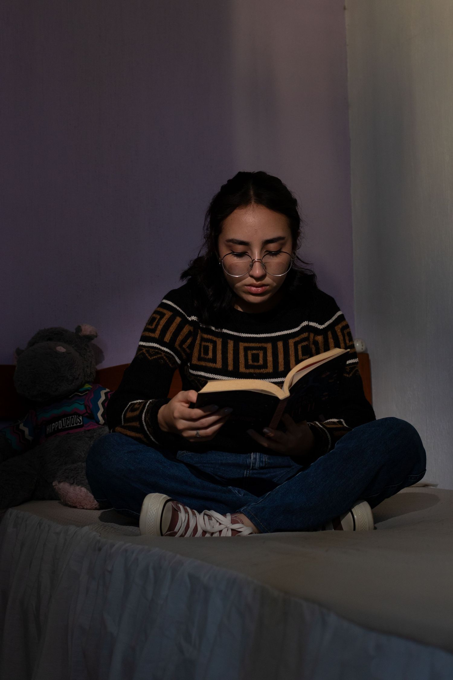 Reader relaxing on bed with book in cozy lighting wearing patterned sweater.