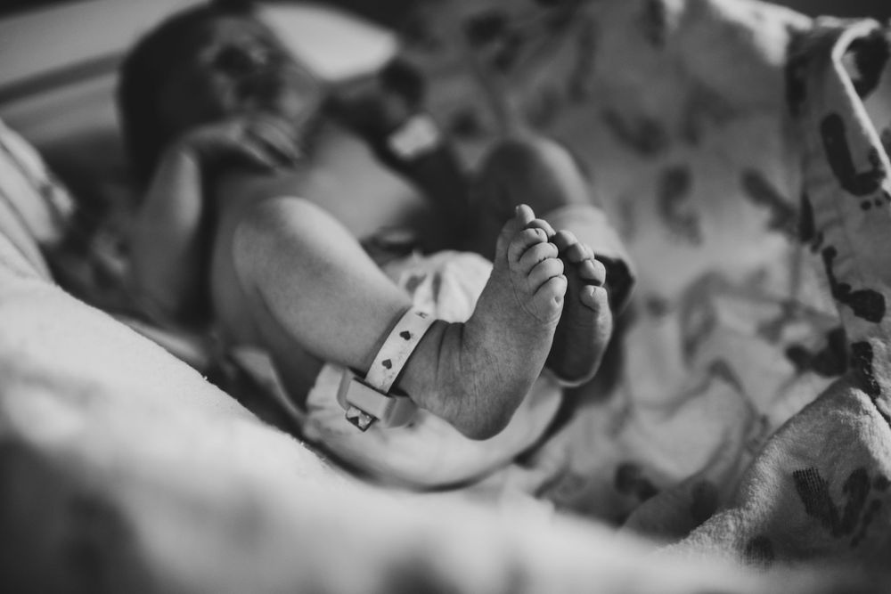 Black and white close-up of newborn baby feet with hospital ID bracelet resting on floral blanket.