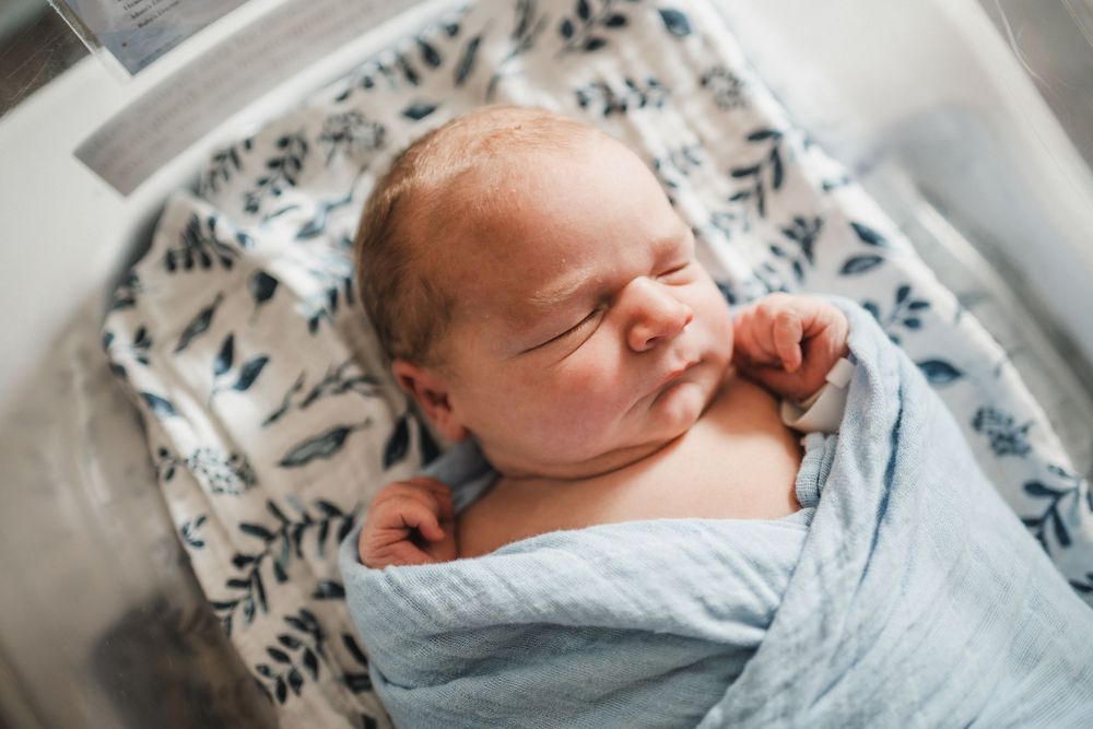 Newborn baby peacefully sleeping while swaddled in light blue blanket with black and white patterned background.