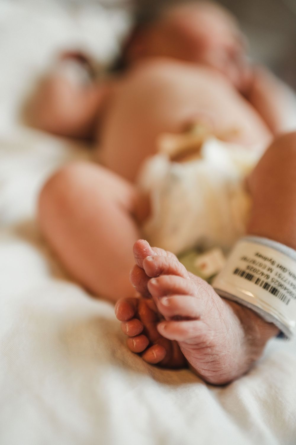 Tiny newborn baby feet resting on white hospital blanket.