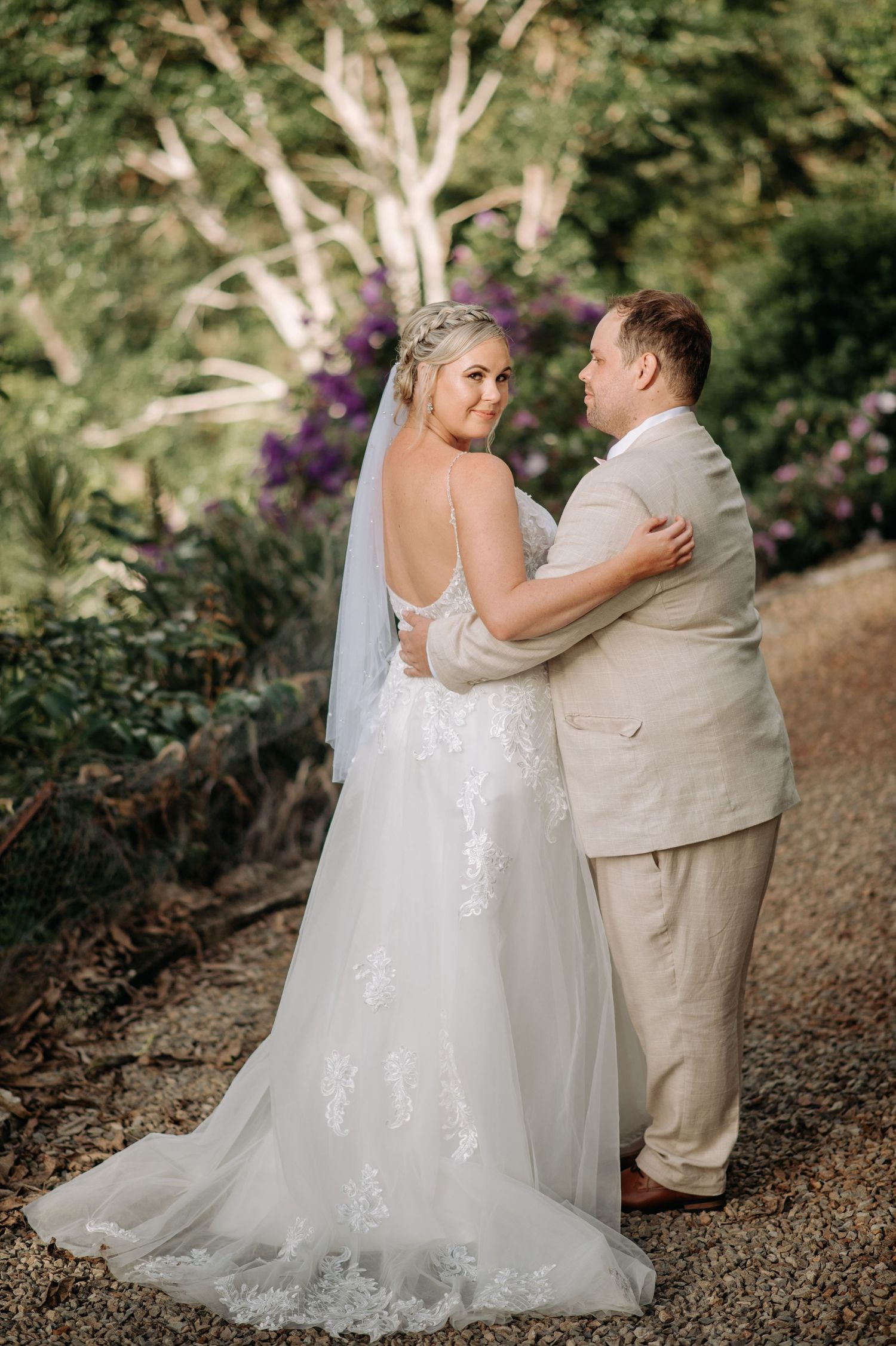 Wedding couple poses on a garden path with beautiful purple flowers in the background.