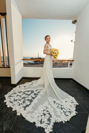 Bride in elegant lace train wedding dress holding yellow bouquet.