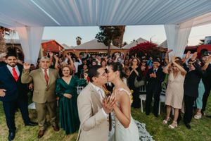 Wedding couple kissing while guests celebrate at outdoor ceremony.