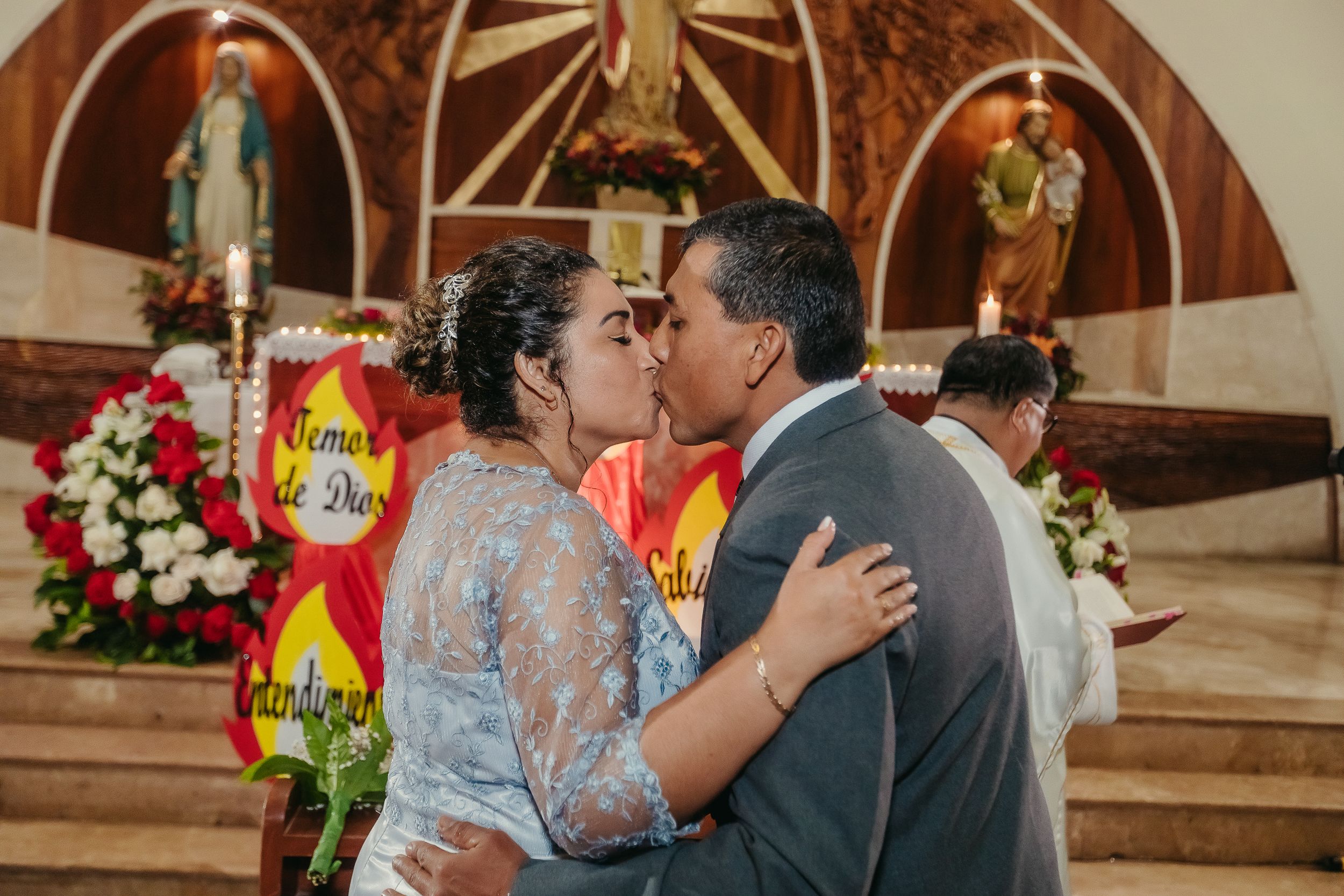 Wedding couple shares a romantic kiss at the altar during their church ceremony with floral decorations.