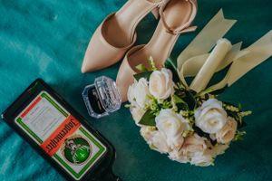 Wedding details featuring beige heels, white roses, and perfume bottle on teal surface.