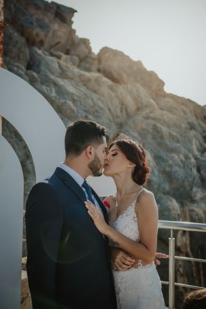 Newlyweds share an intimate moment against a dramatic rocky cliff backdrop.