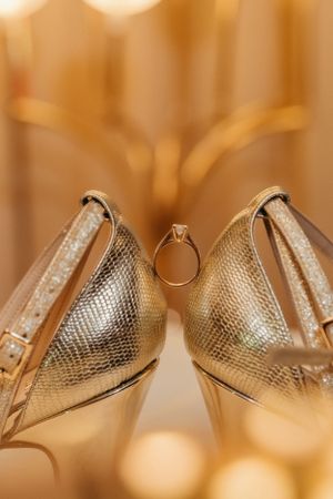 Diamond engagement ring nestled between a pair of sparkly gold wedding shoes.