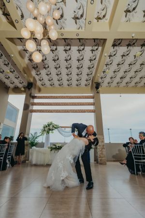 Couple performs romantic dance dip under ornate chandelier at wedding reception.