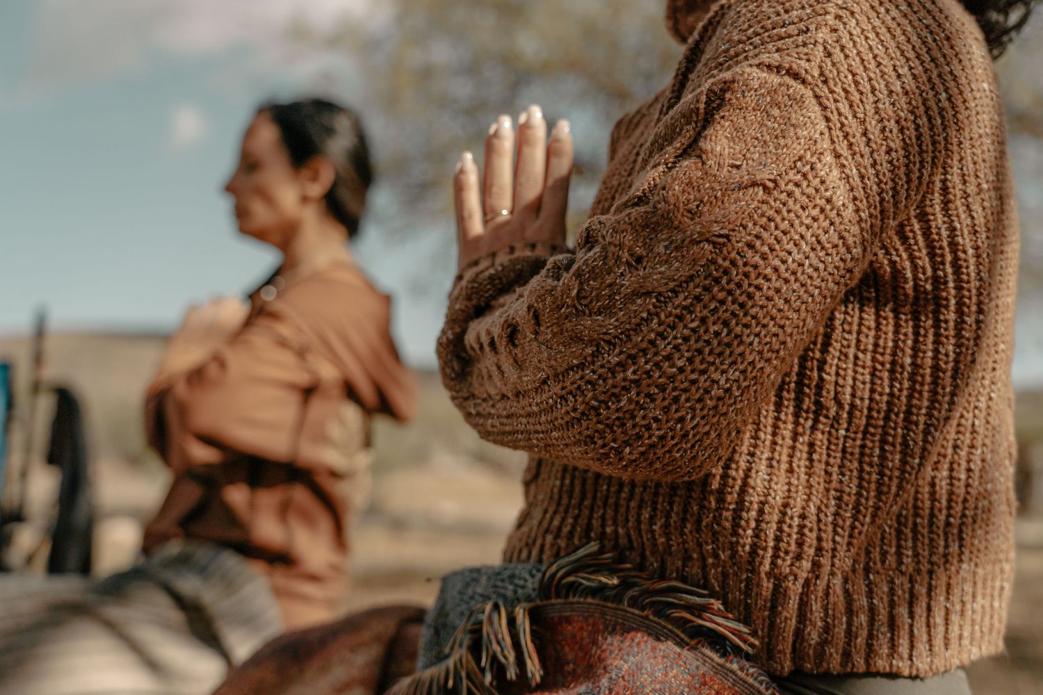Two riders wearing warm sweaters on horseback in desert setting.