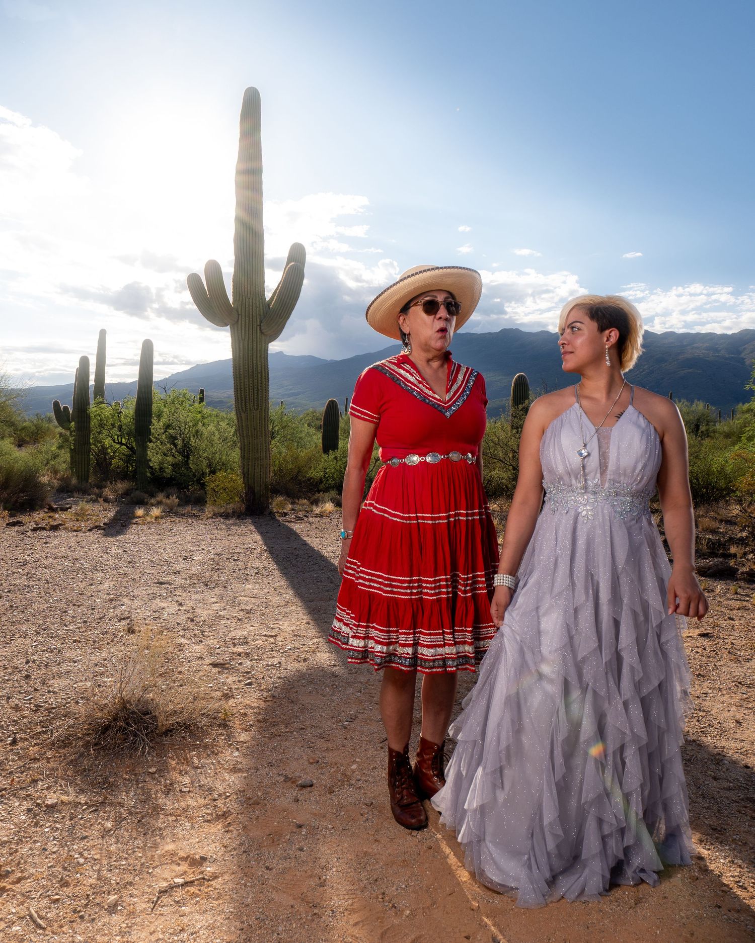 Two women in flowy dresses posing in front of desert saguaro cactus landscape.
