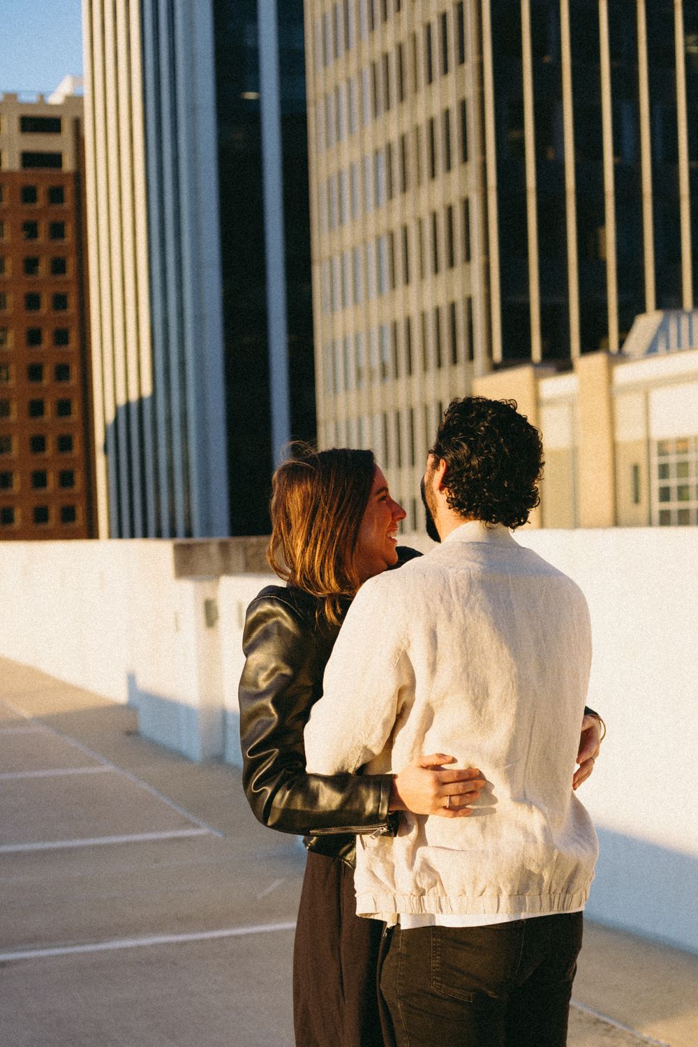 A woman hugs her fiancé in a parking garage as the sun rises.
