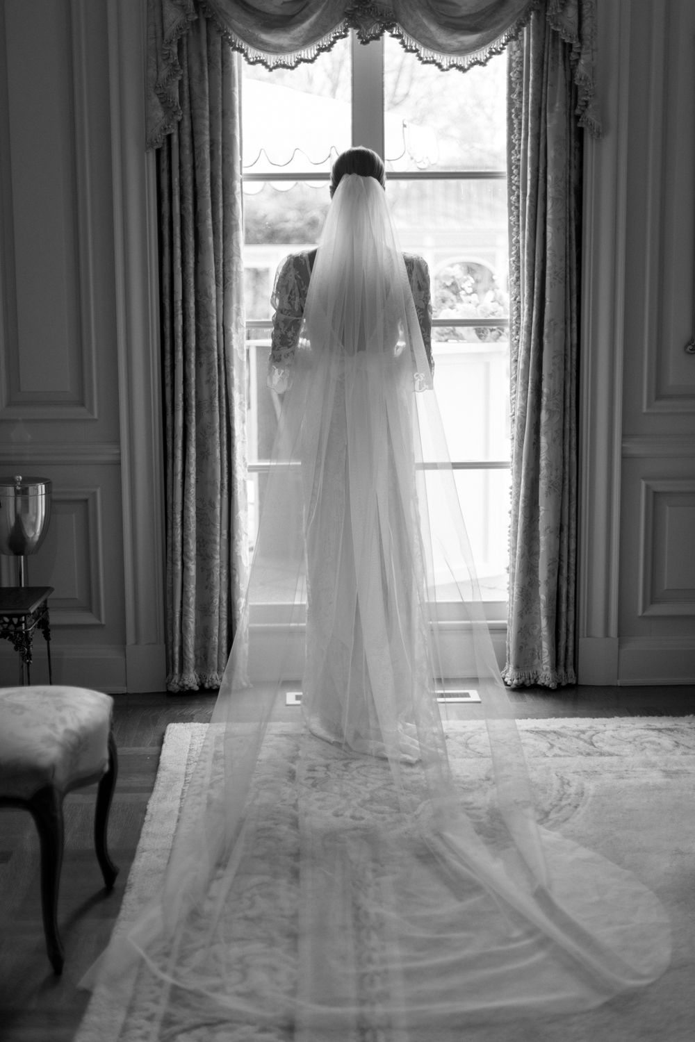 Bride with long classic veil looks out the window. Black and white.