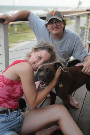 Young married couple poses casually with their dog on the balcony.