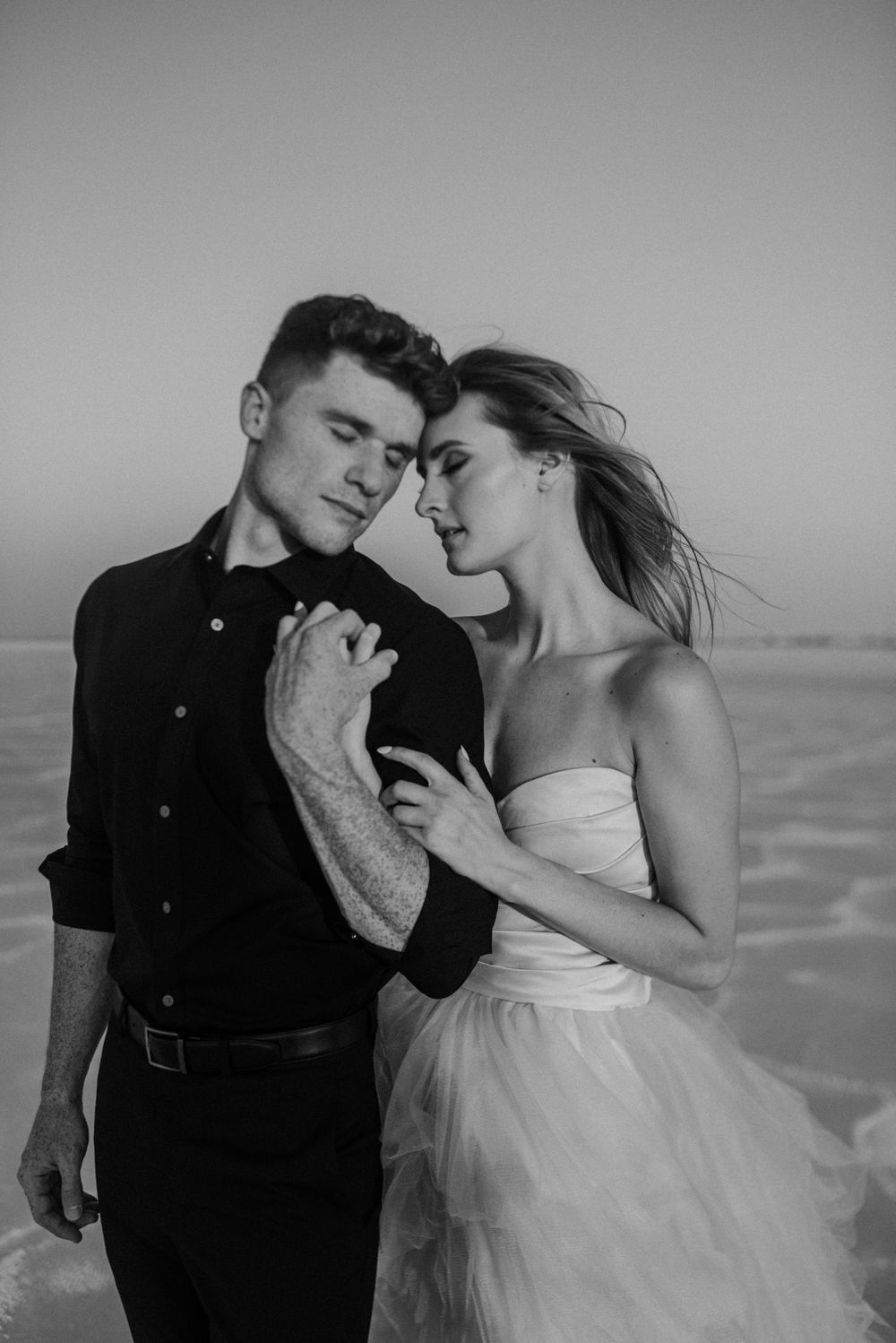 A black and white portrait of a couple in formal wear on a salt flat landscape.