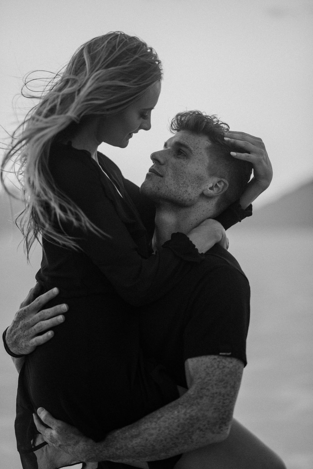 An intimate black and white portrait of a couple embracing outdoors.