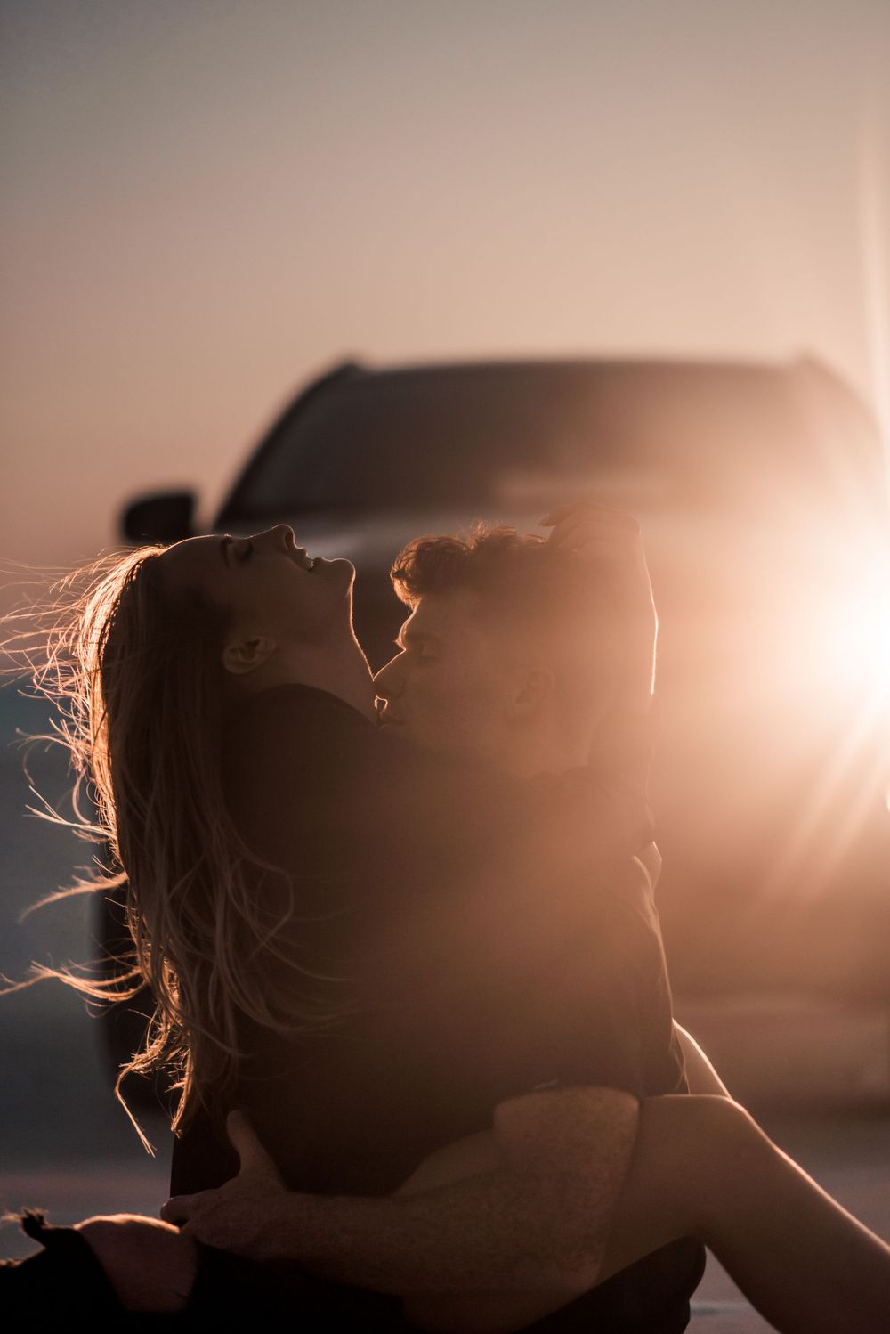 A backlit silhouette portrait against sunset with wind-swept hair and soft lighting.