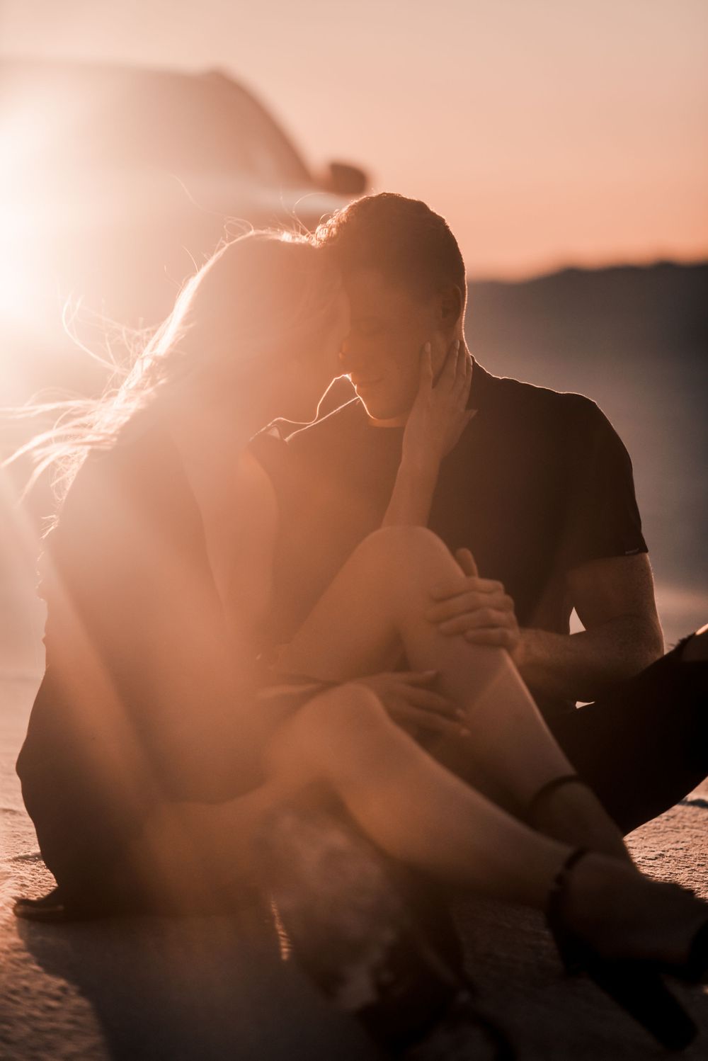 Intimate couple moment captured in warm sunlight on desert terrain.