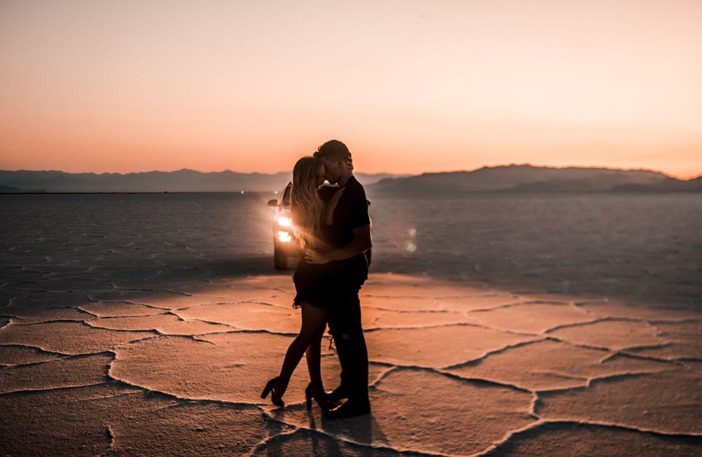 Couple embracing on cracked salt flats during golden sunset.