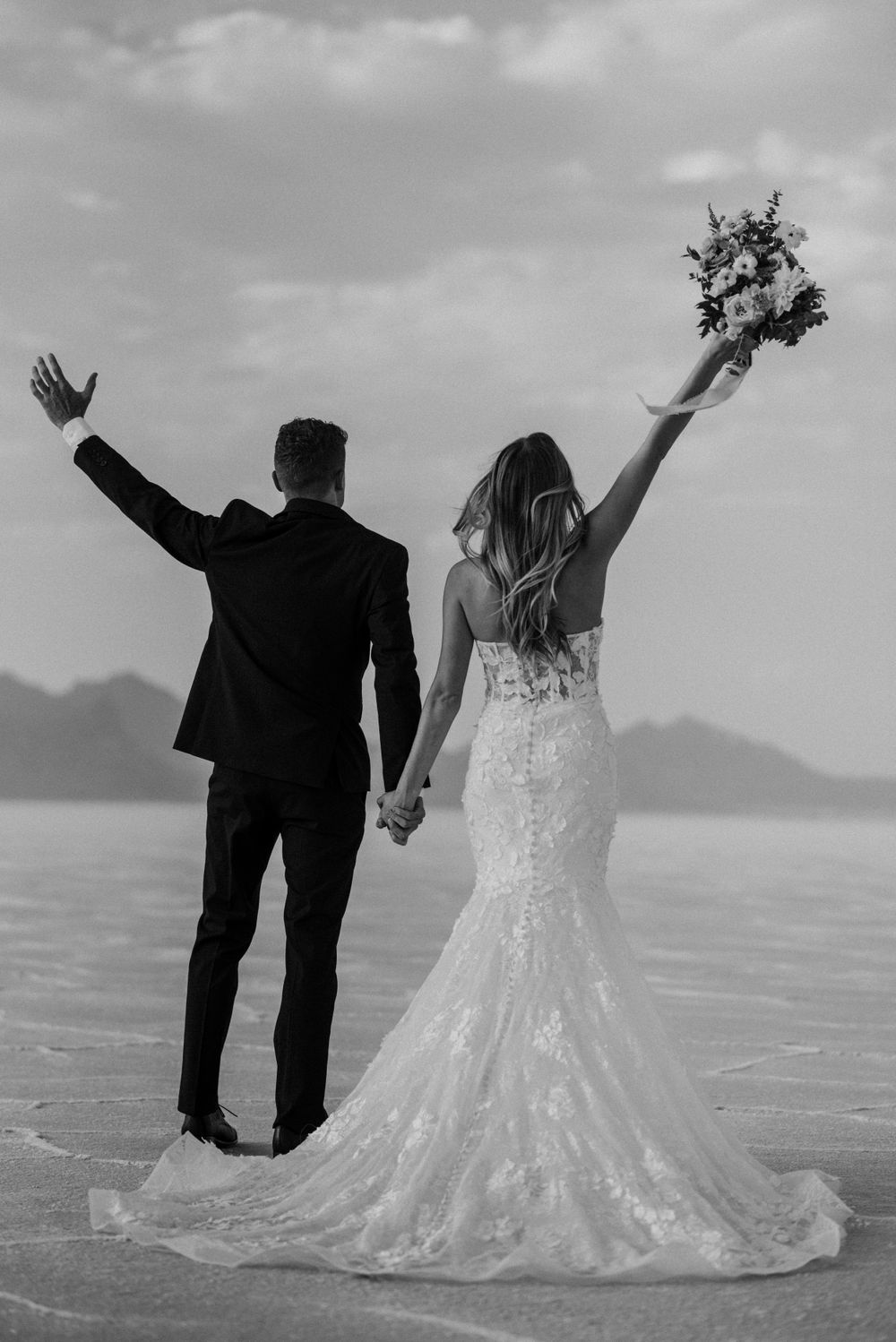 Newlyweds celebrating with raised arms on salt flats during their wedding photoshoot.