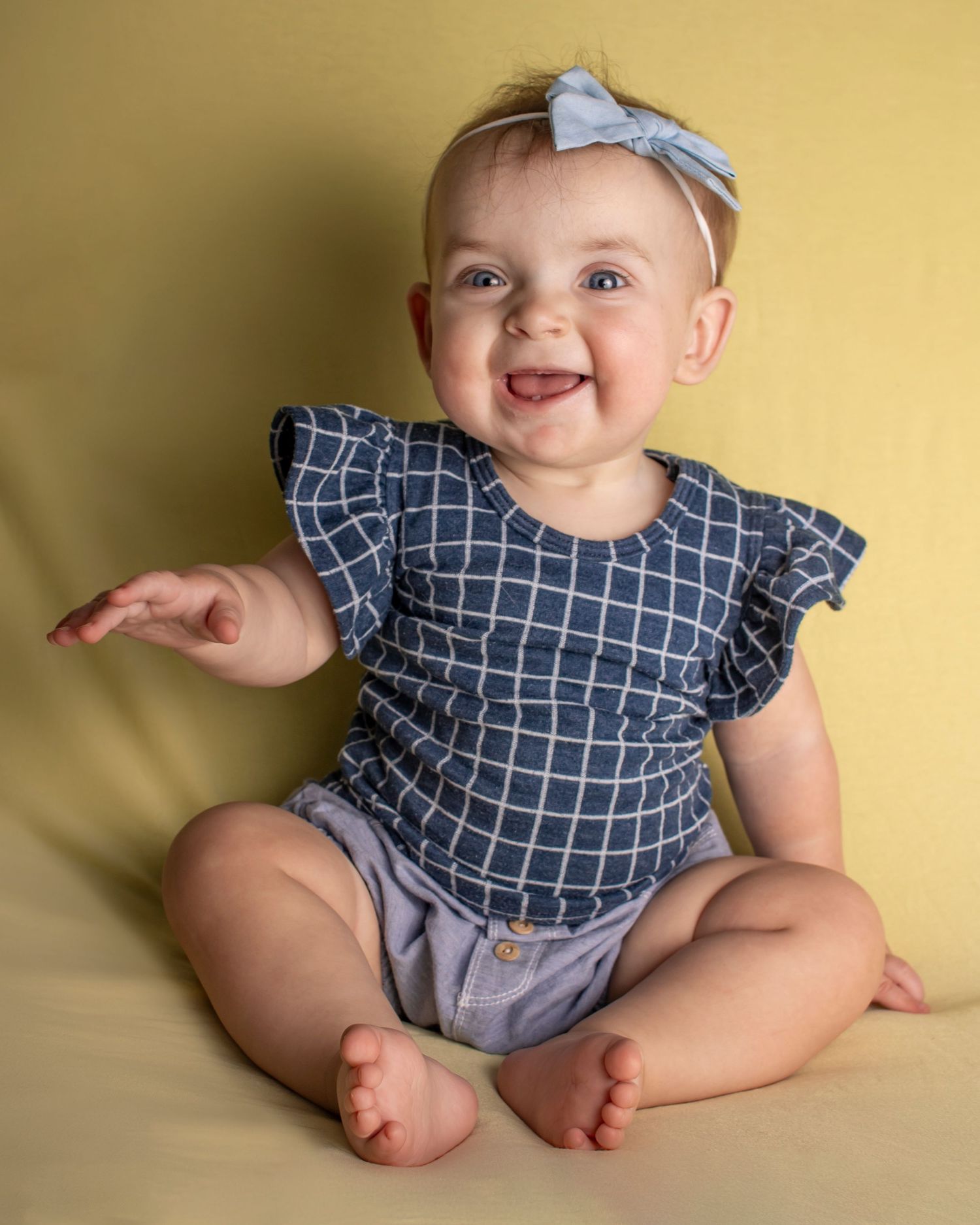 A wide smile on a chubby baby who is sitting on a yellow background