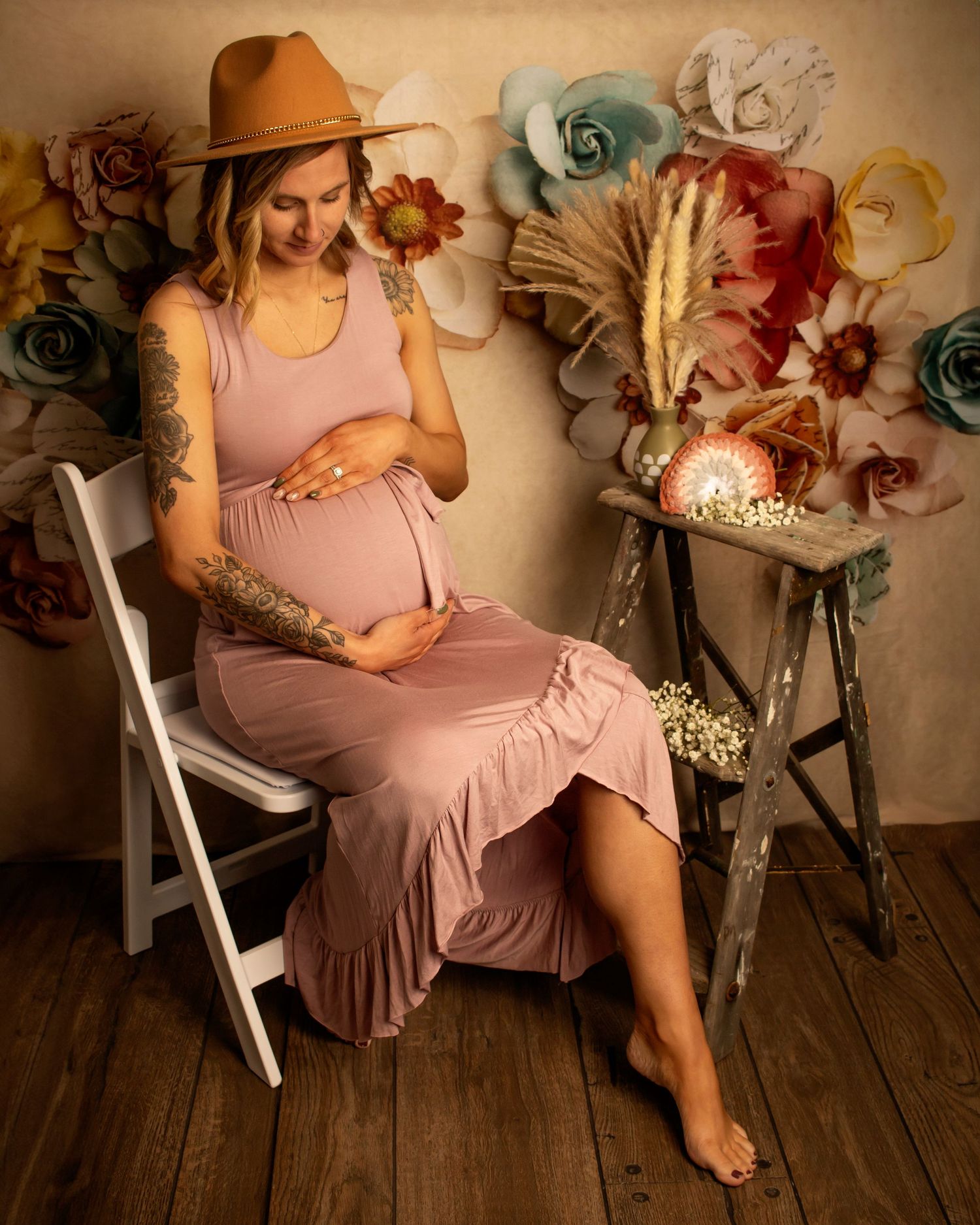 A visibly pregnant mother looks down at her cradled stomach. The entire scene is styled with a boho aesthetic.