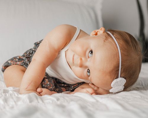 A young girl with visible facial differences lays over with a sly smile as she plays on a bed.