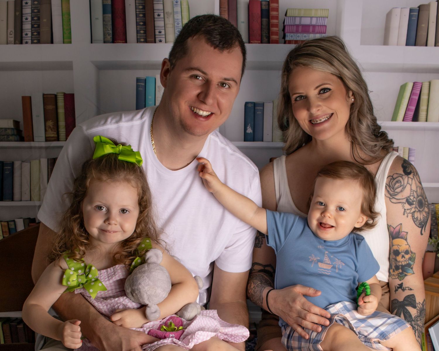 A family of four sits and smiles at the camera in front of bookshelves