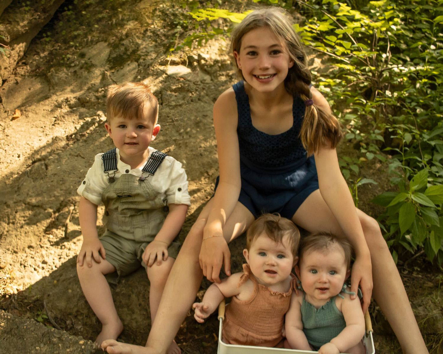 Four siblings look at the camera from where they are seated on a creek bank