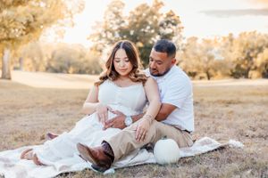 A couple sits together on a white blanket in a sun-drenched field during a romantic outdoor photoshoot.