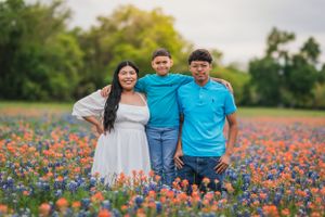 Three people pose together in a vibrant field of orange and blue wildflowers during golden hour.