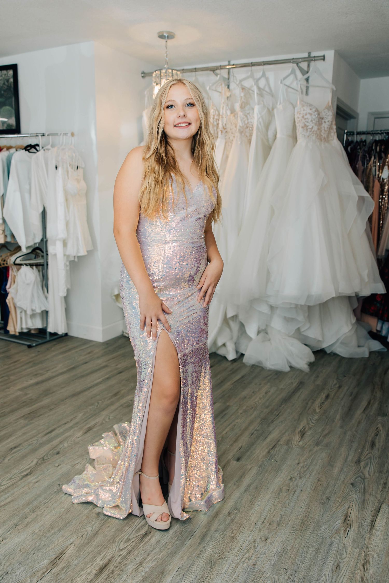 Young woman in iridescent sequin slit gown posing in bridal and prom dress boutique.