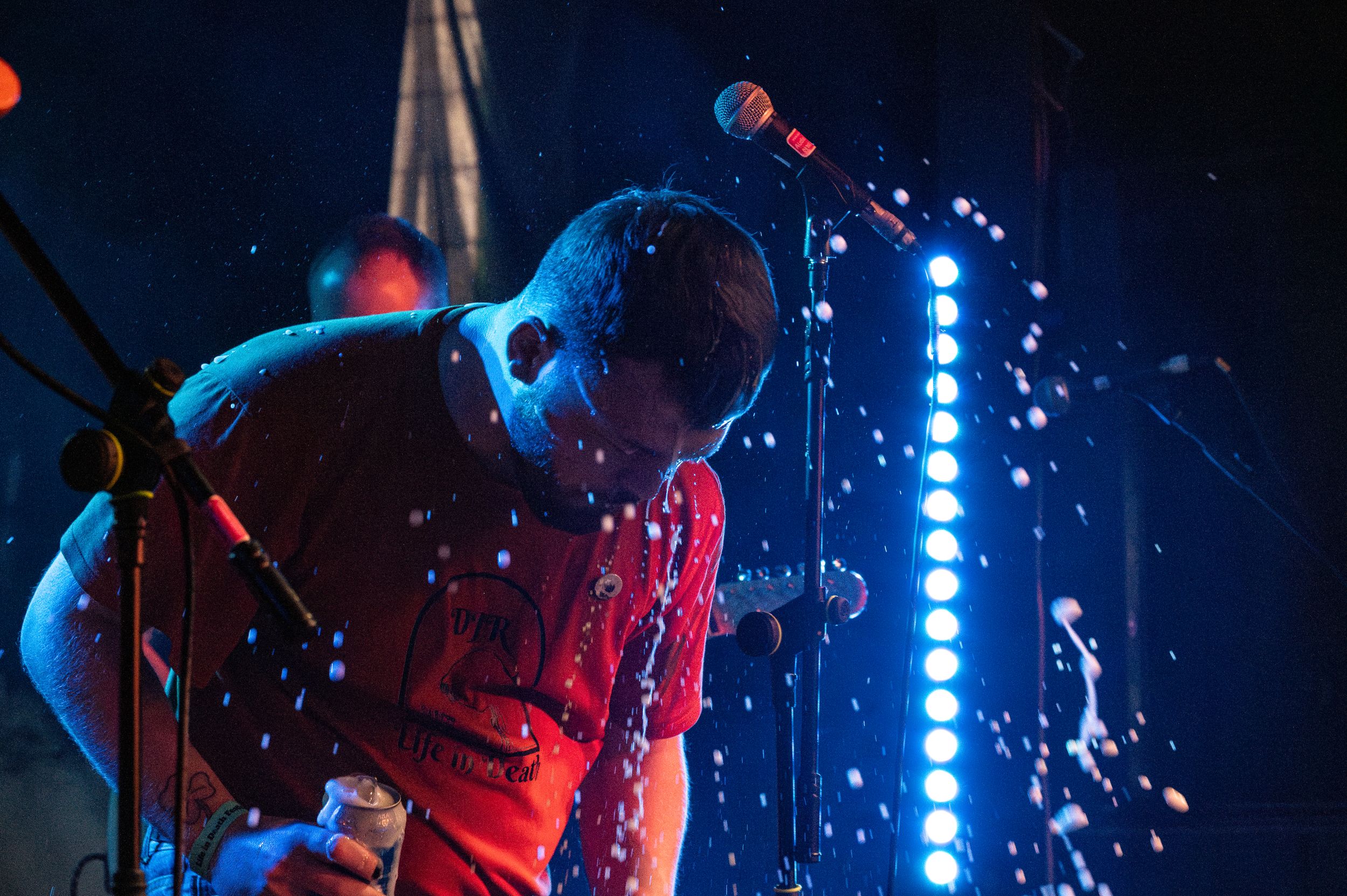 Musician bathed in red and blue stage lighting performs with guitar.