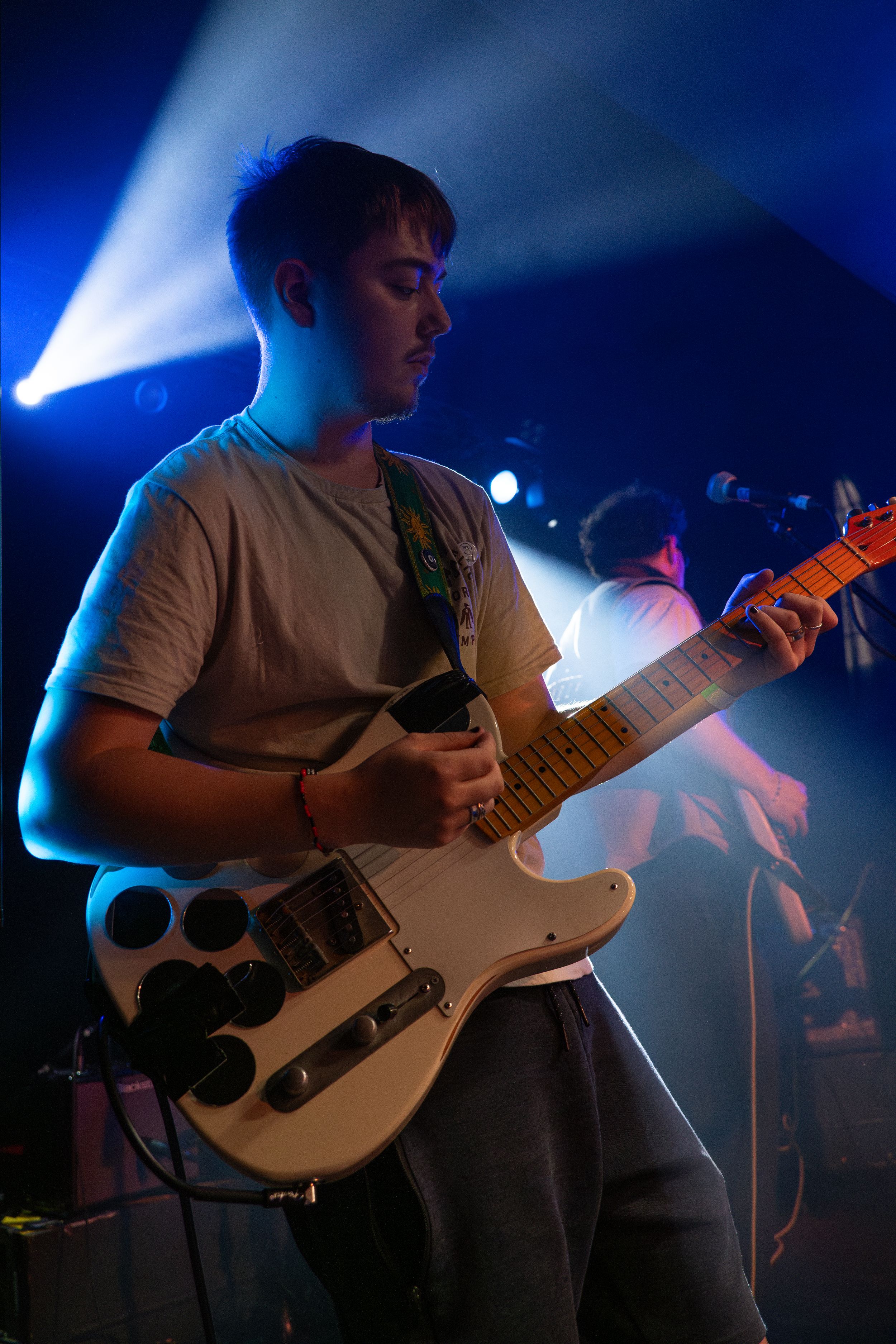Guitarist playing white electric guitar under dramatic blue stage lighting.