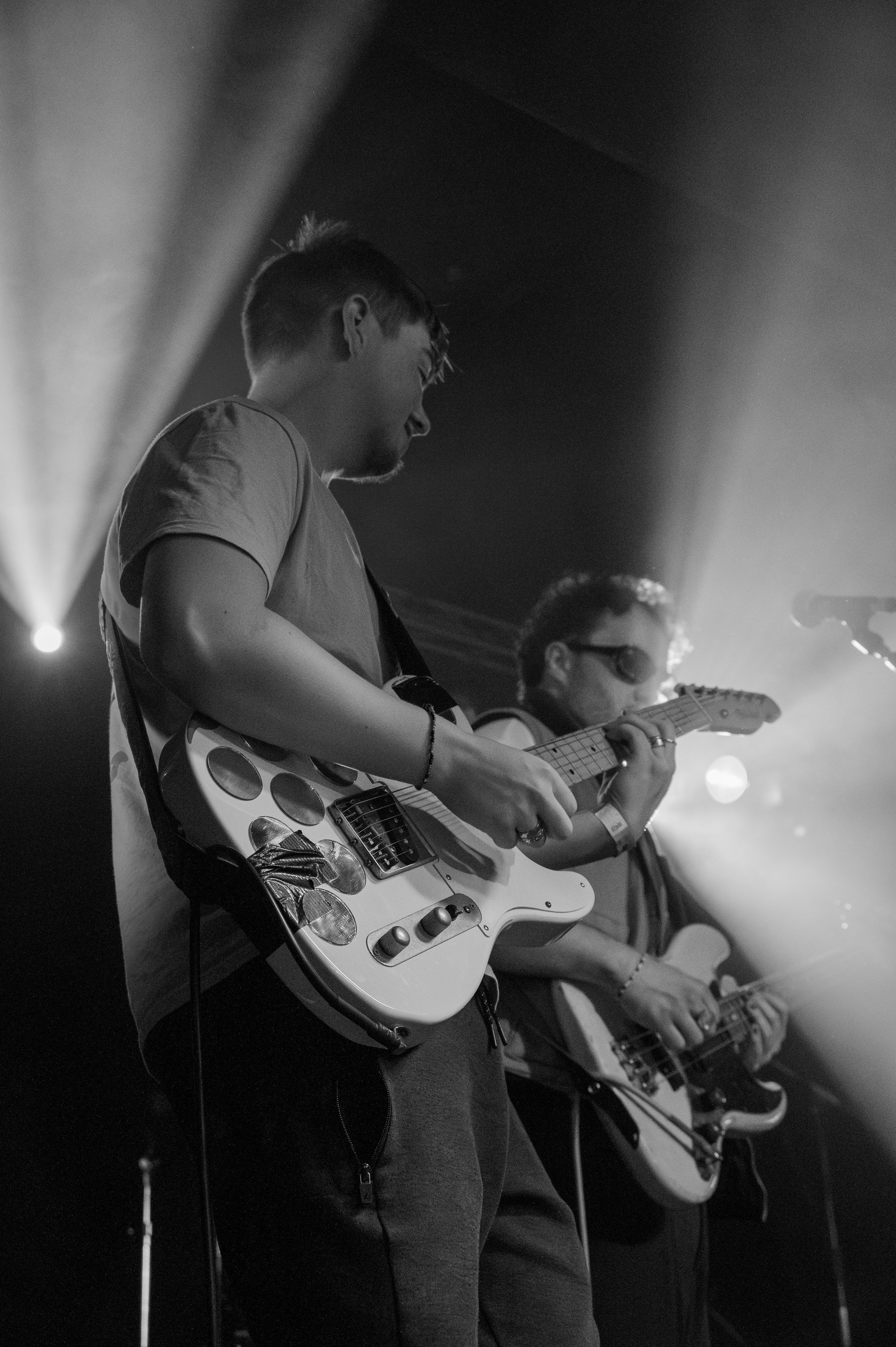 Black and white photo of guitarists performing on stage with dramatic lighting.