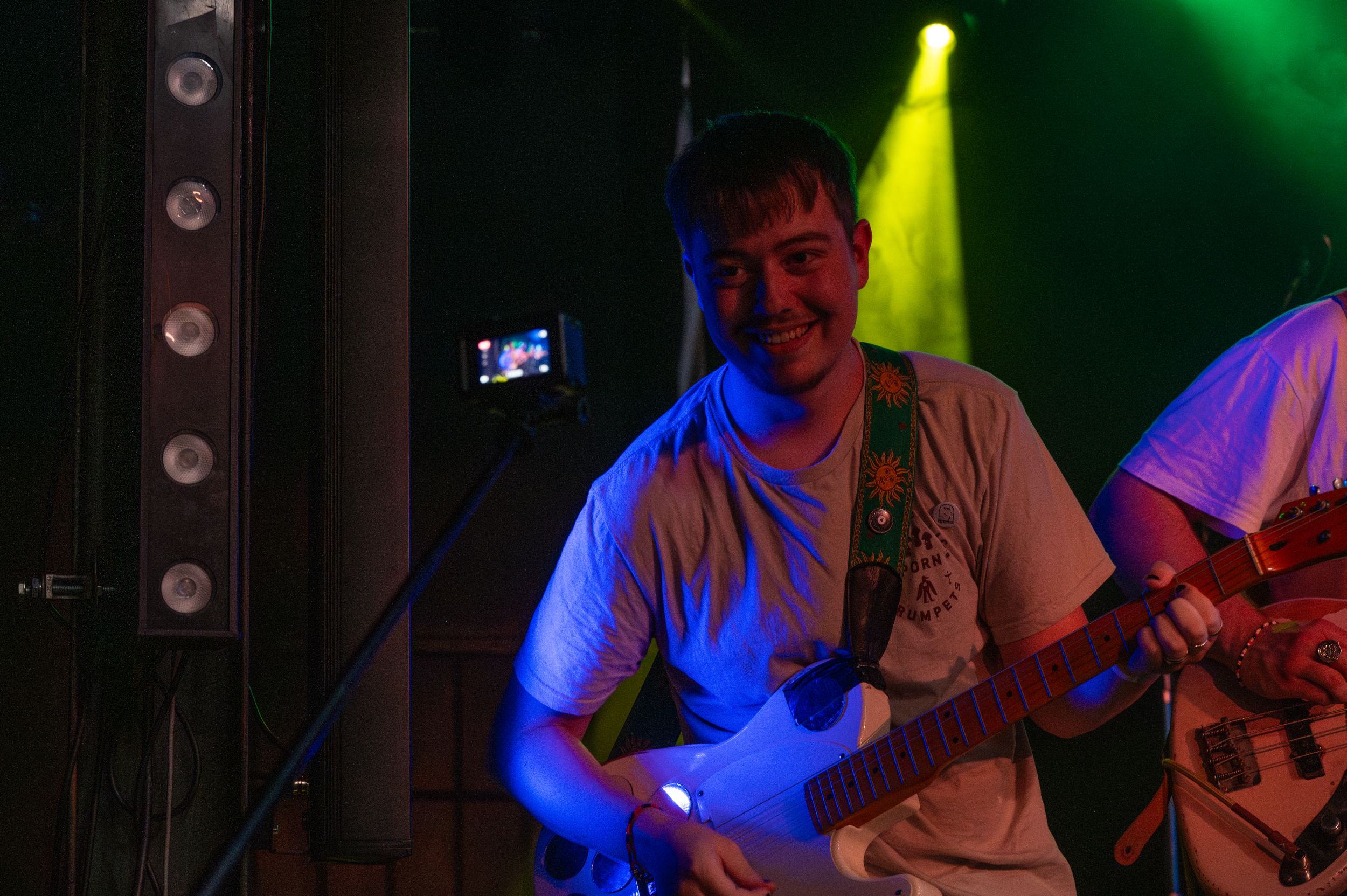 Musician performs with guitar on dimly lit stage with dramatic blue and yellow lighting effects.