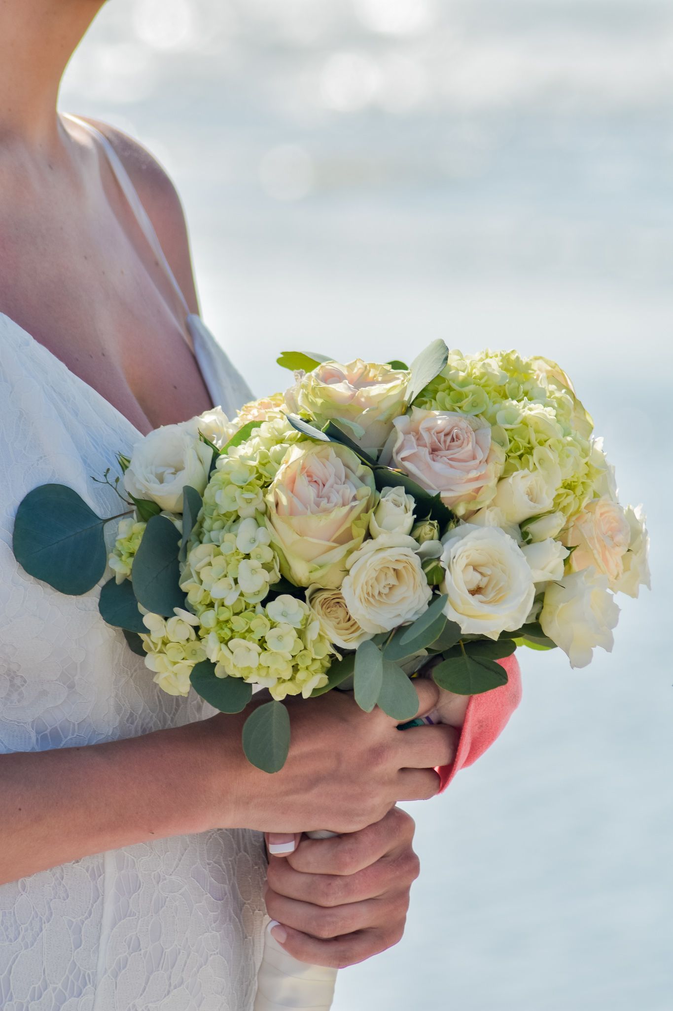 Beautiful white and cream wedding bouquet with roses and hydrangeas against ocean backdrop.