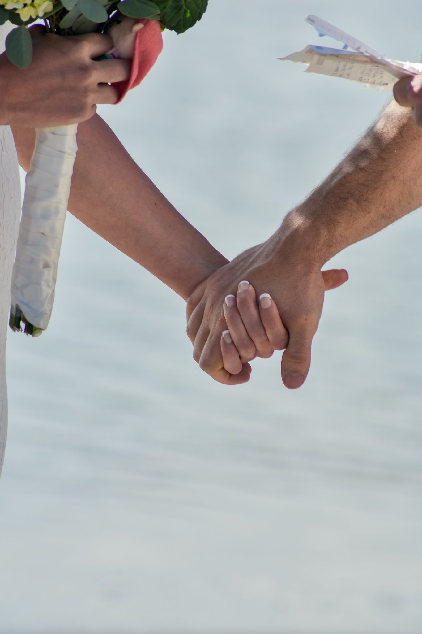 Intimate moment of newlyweds holding hands while holding a wedding bouquet.