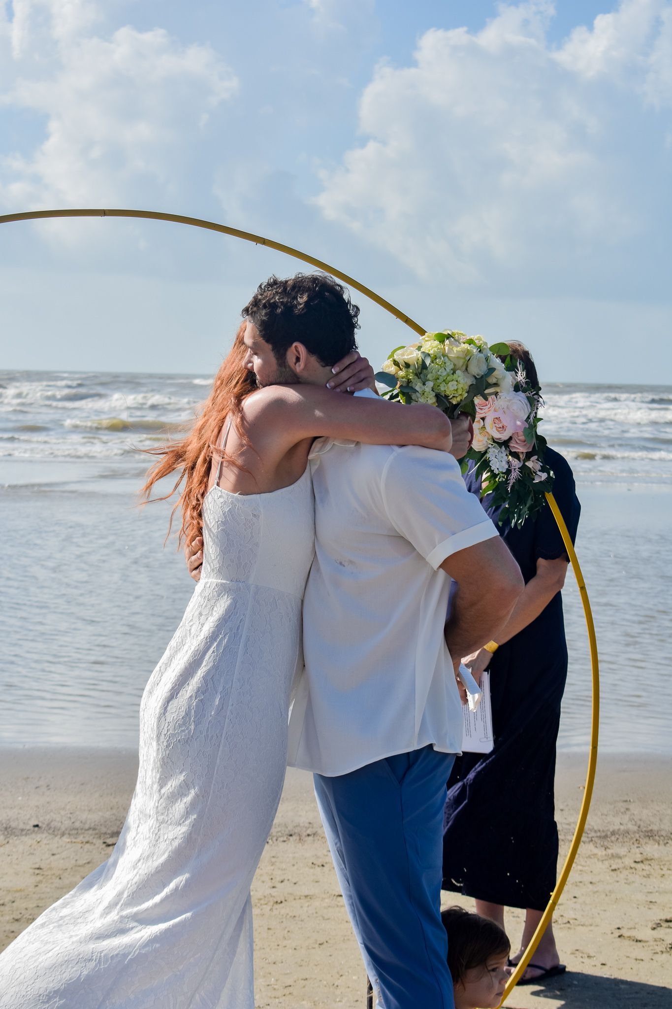 Beach wedding ceremony under a golden arch with ocean waves in the background.