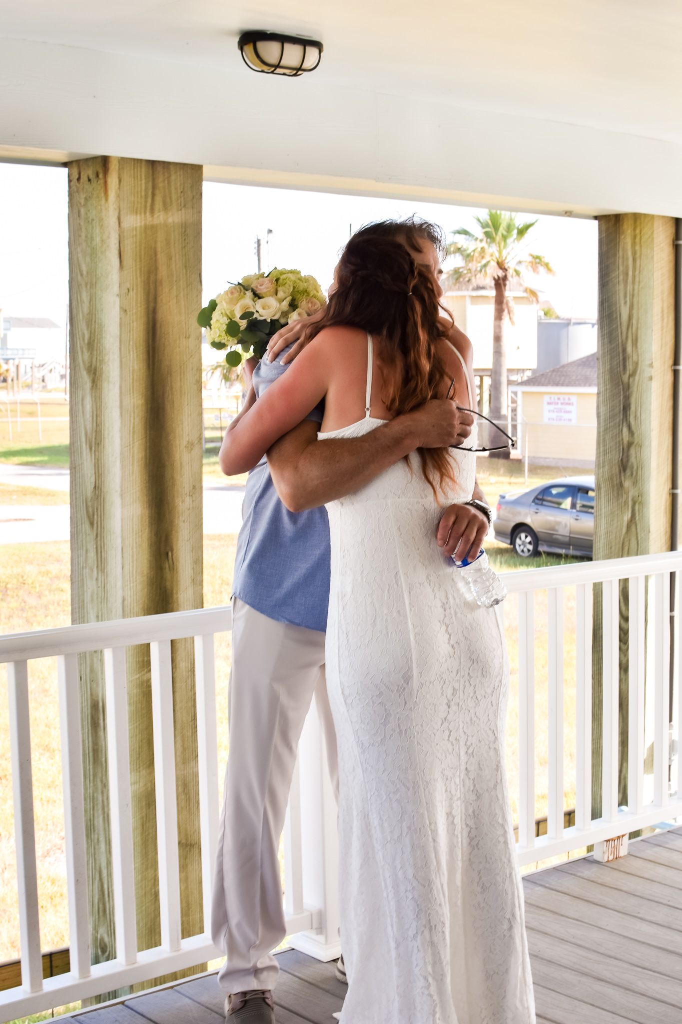 Emotional embrace on a white porch with palm trees visible in background.
