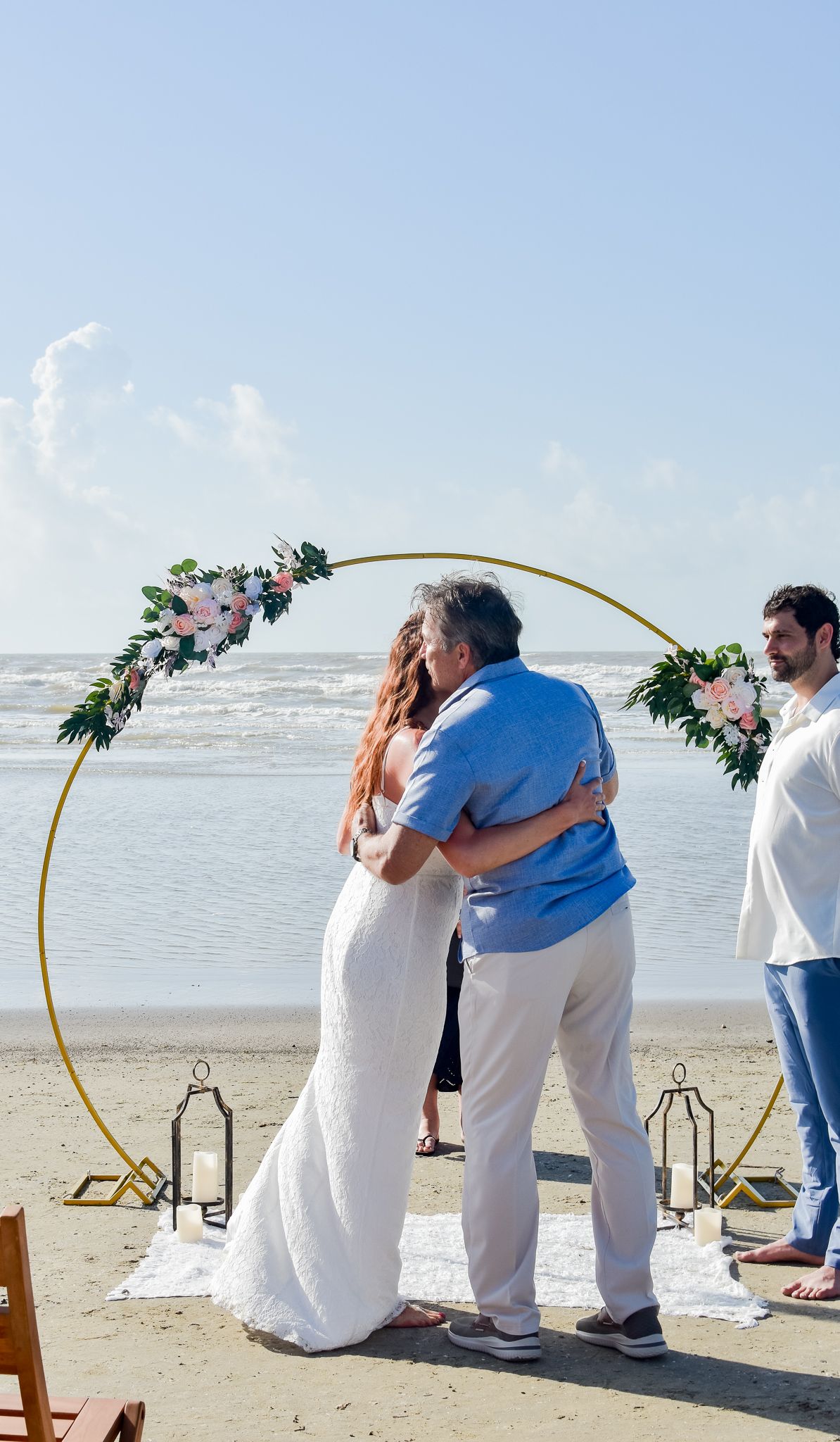 Wedding ceremony moment on the beach with an elegant floral arch and lanterns on the sand.