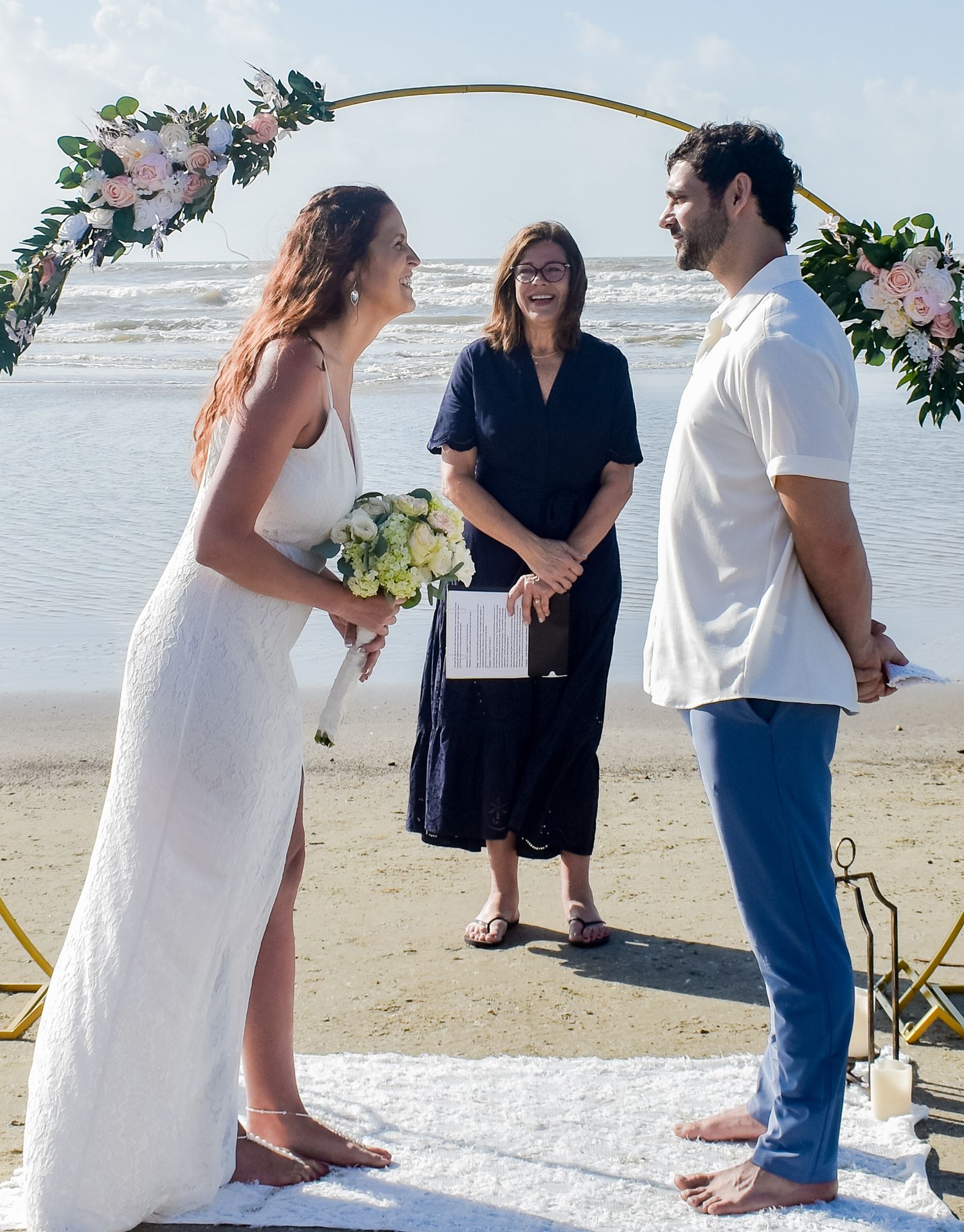 Joyful moment during beach wedding ceremony under decorated golden arch with waves behind.