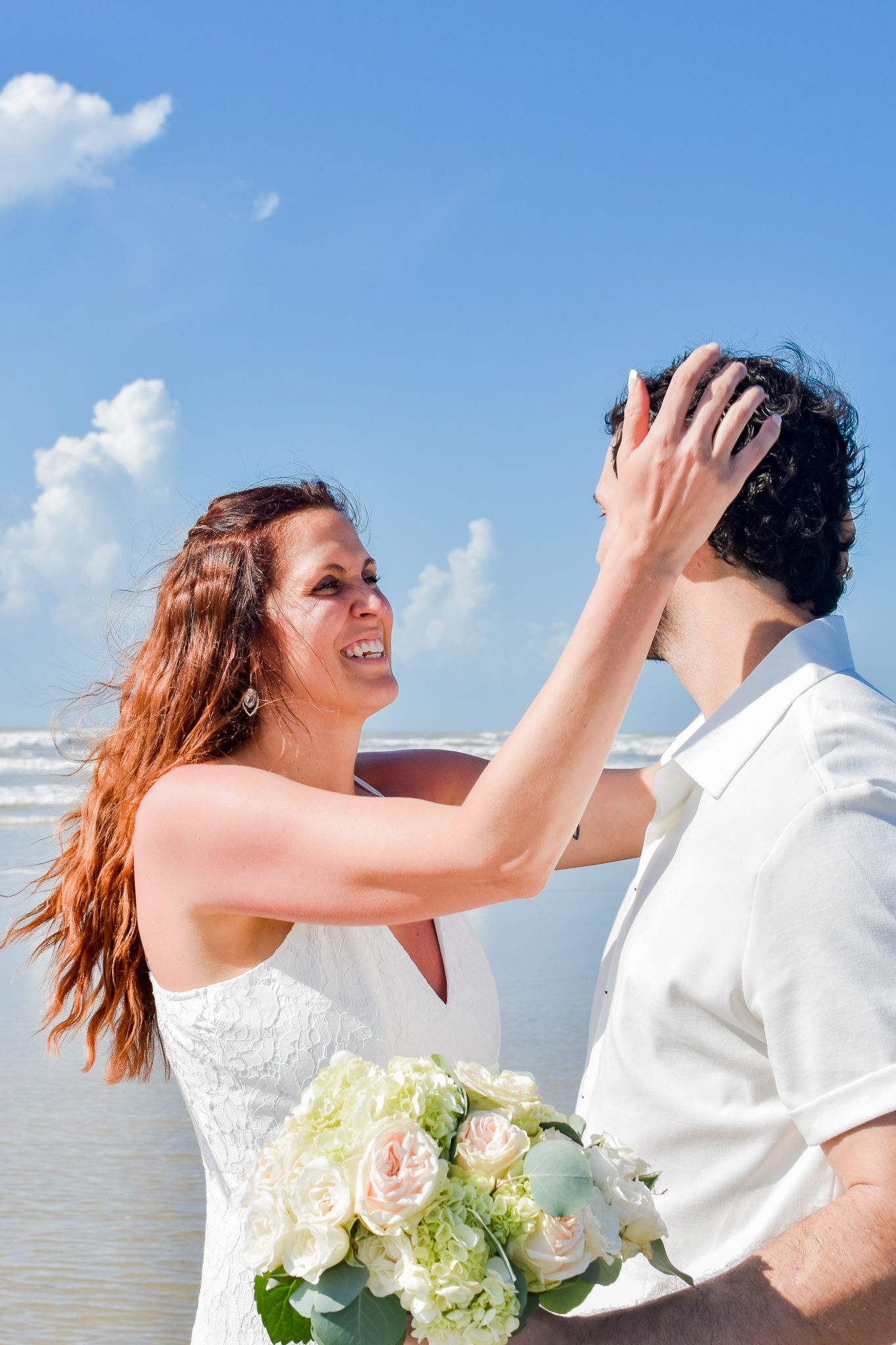 Wedding couple shares romantic moment on beach with bouquet of white roses.