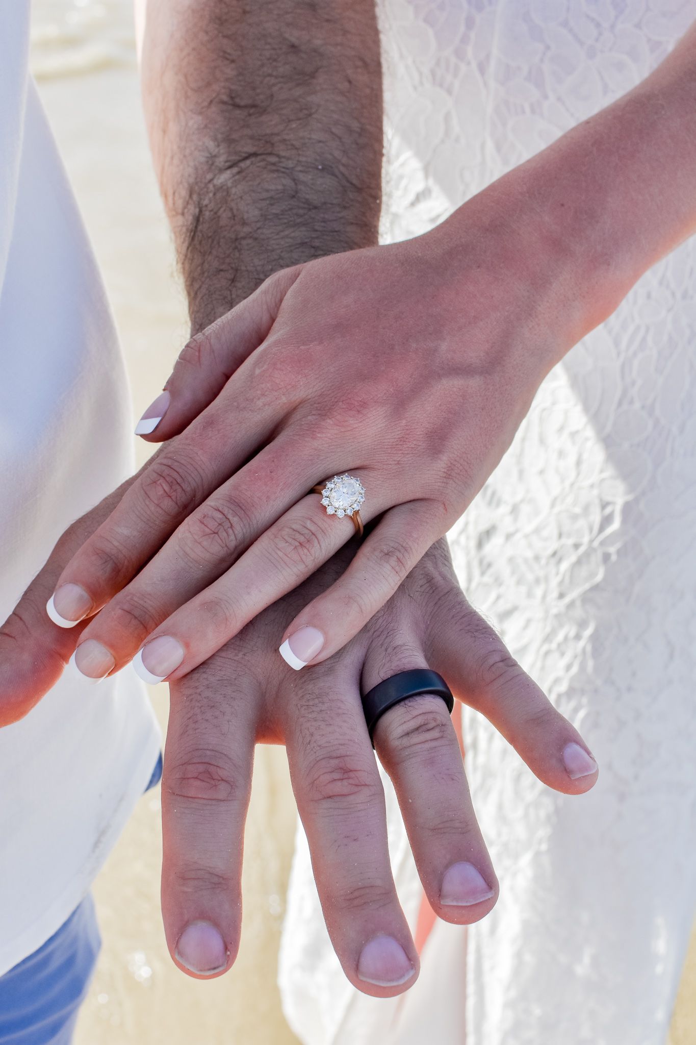 Close up of newlywed couple's hands showing wedding rings against white fabric.