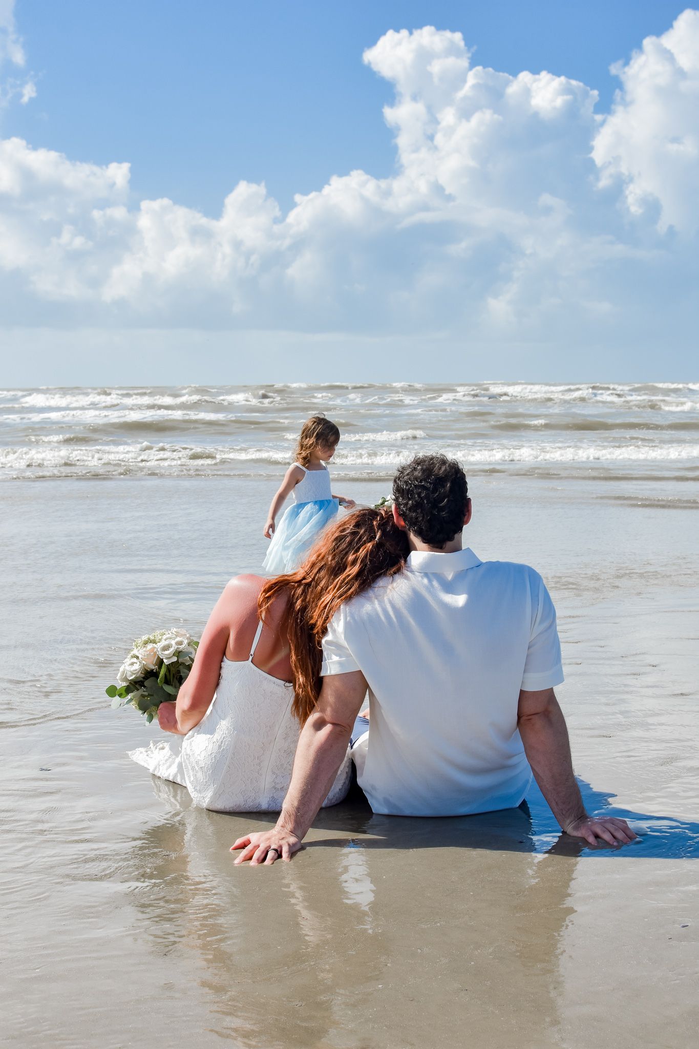 Family sitting together on beach watching waves as ocean surf rolls in.