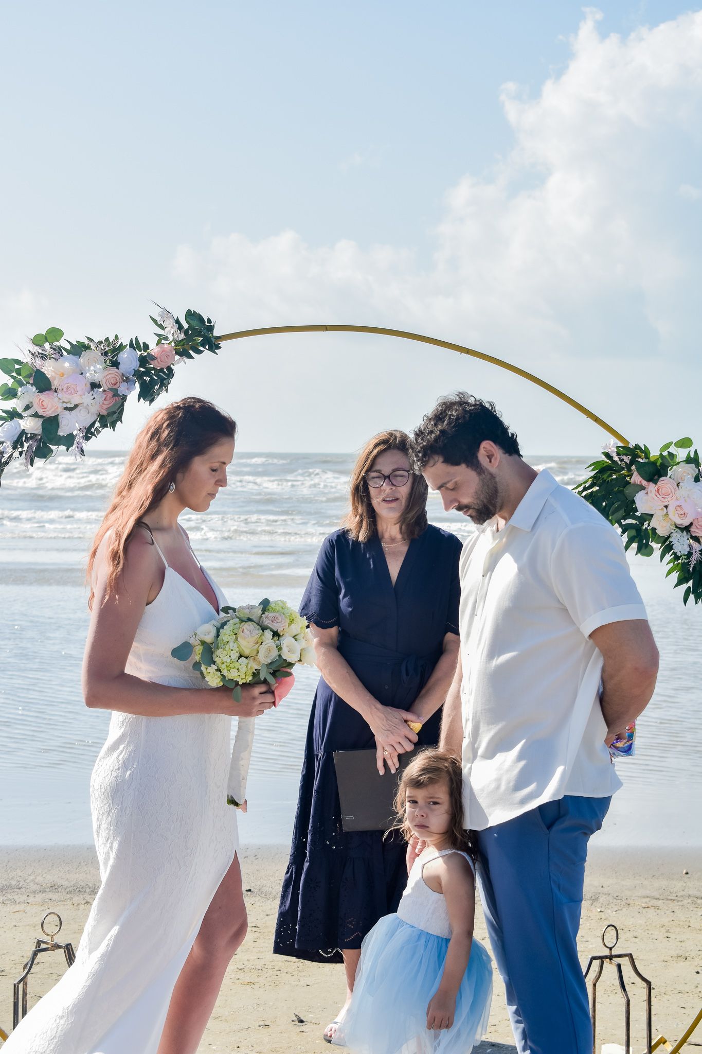 Wedding ceremony on beach with floral arch backdrop and ocean waves in background.