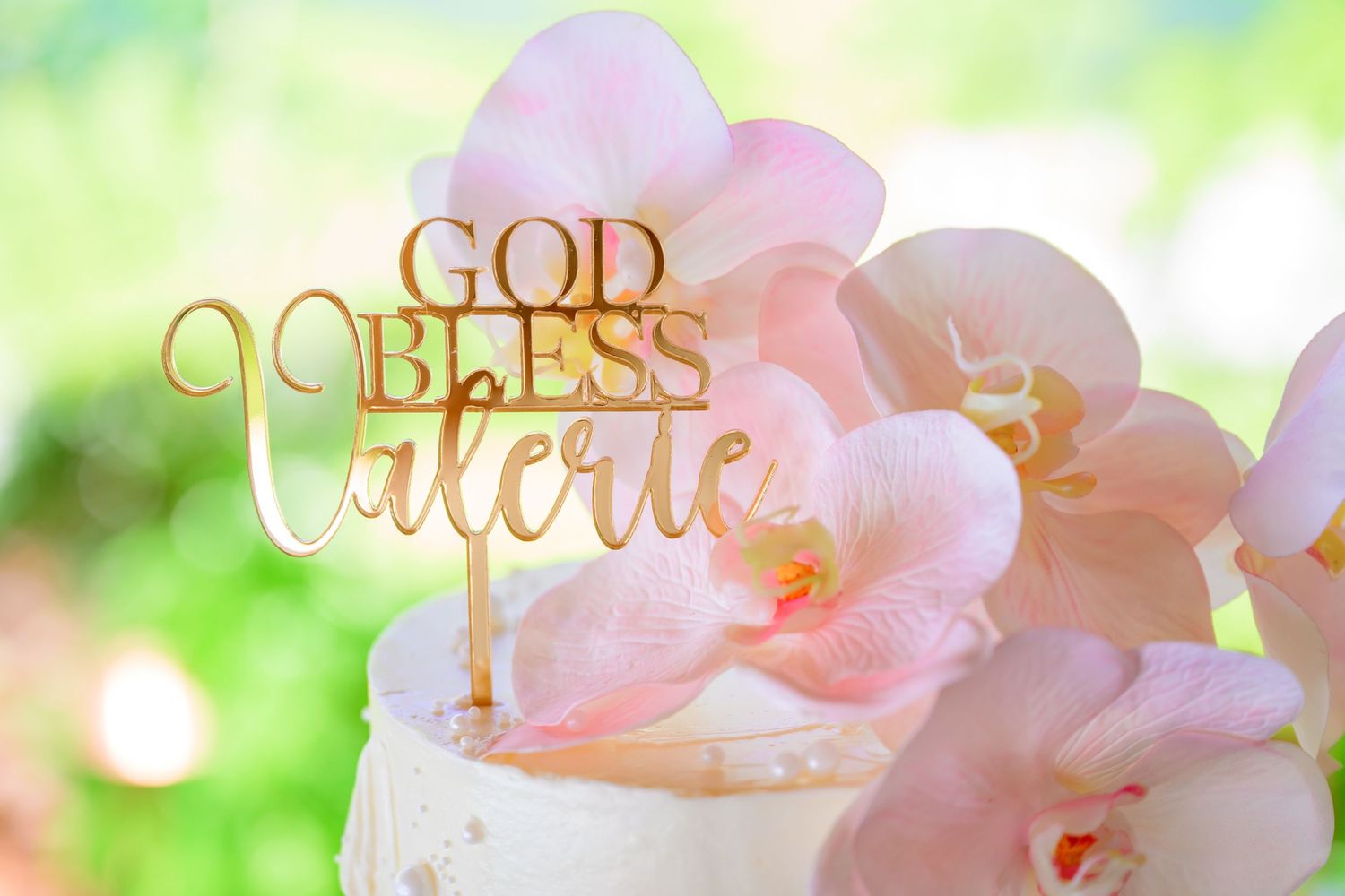 Gold 'God Bless' text overlay on soft pink floral background with bokeh effect.