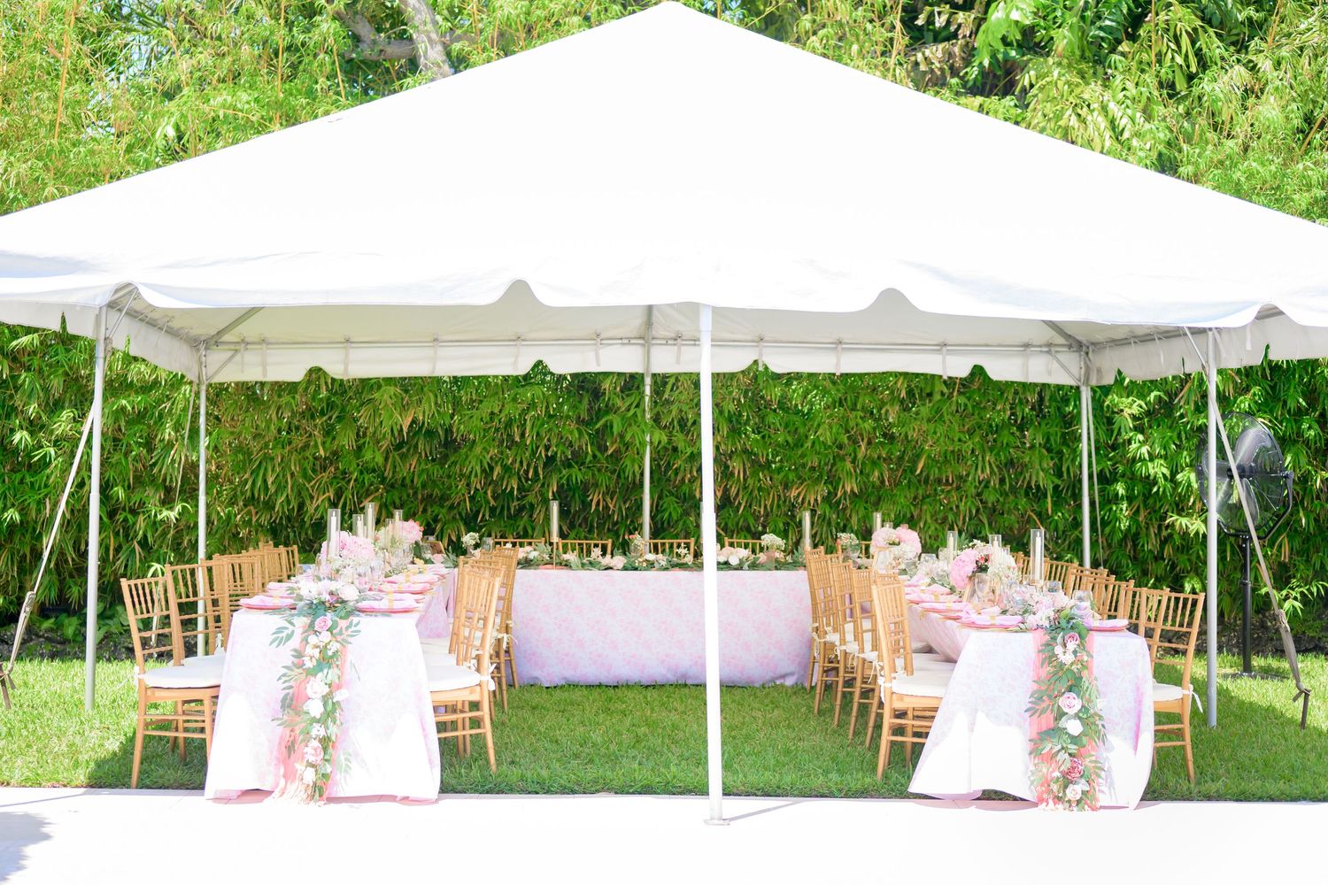 White event tent set up outdoors with elegant table settings and chairs.