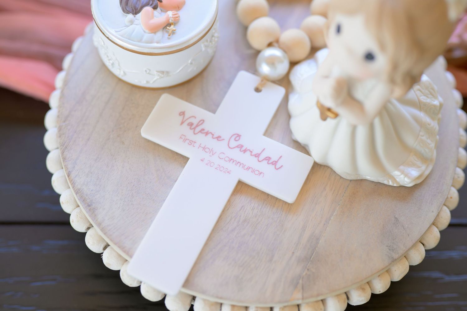 A white decorative cross placed on a wooden scalloped tray with white pearls and vintage decor elements.