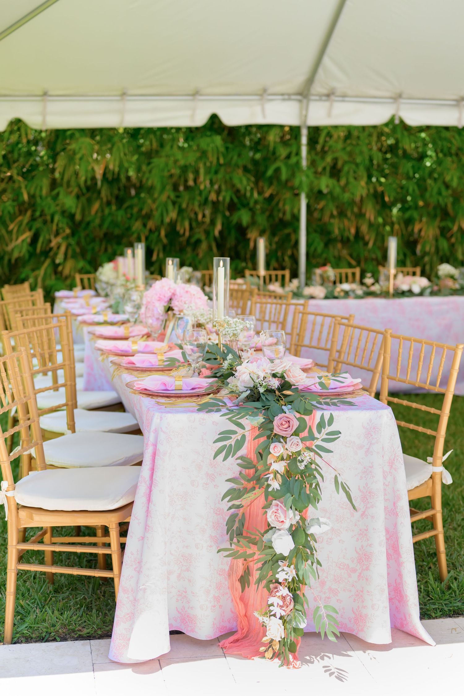 Elegant outdoor wedding reception table with pink linens and floral centerpiece under a white tent.