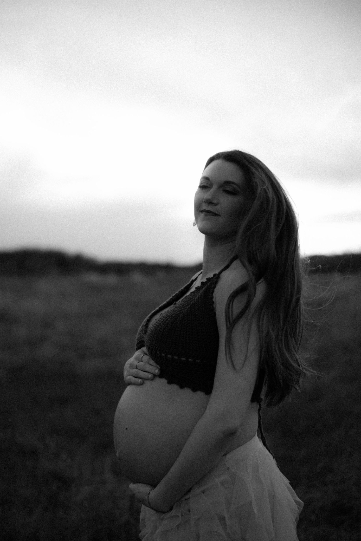 Artistic black and white maternity photoshoot sequence showing a woman in a field at sunset.